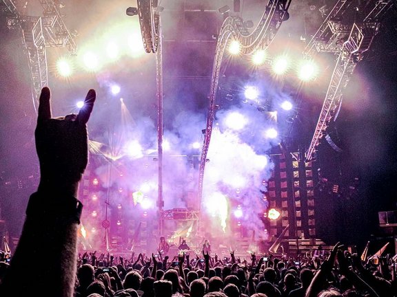 Bild aus der Menge mit Blick auf die Bühne beim Konzert von Alice Cooper & Moetley Crue. Im Vordergrund wird eine Hand in die Luft gehalten, die den kleinen Finger und den Zeigefinger nach oben streckt.